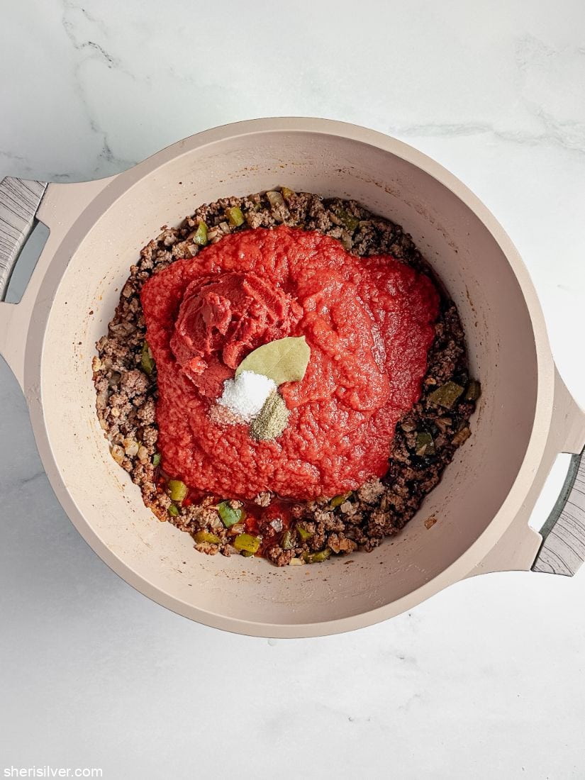 browned ground beef in a pot with tomatoes and tomato paste