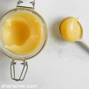 lemon curd in a mason jar next to a white ceramic spoon filled with lemon curd