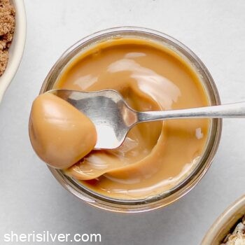 homemade dulce de leche in a glass jar with a silver spoon
