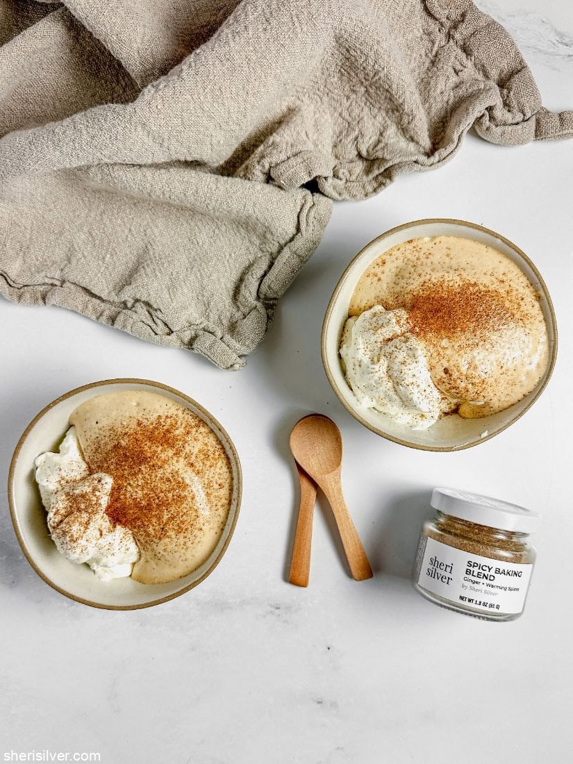 Dalgona mousse and whipped cream in ceramic bowls with wooden spoons and a jar of spice blend