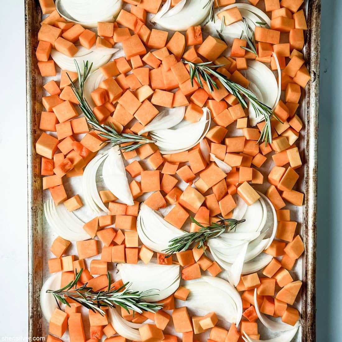 butternut squash on a baking sheet with onions and rosemary