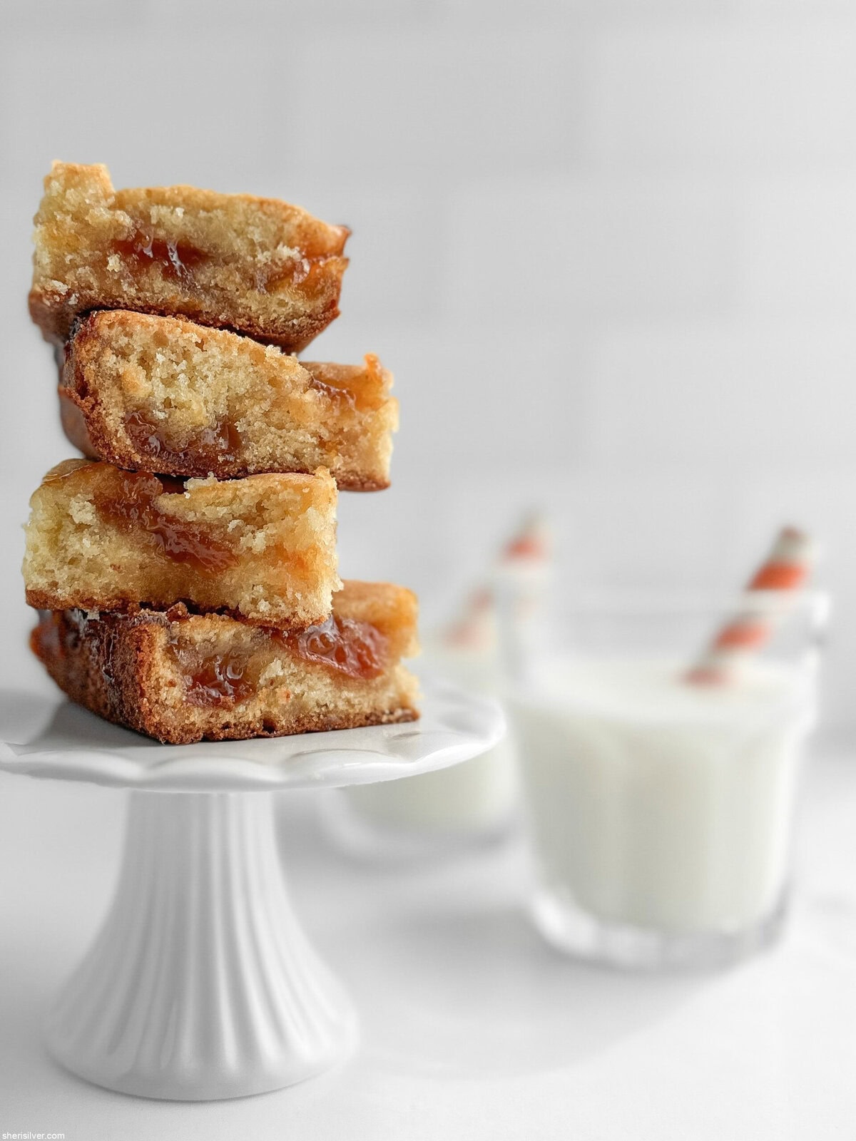 apricot almond bars on a white cake plate with glasses of milk