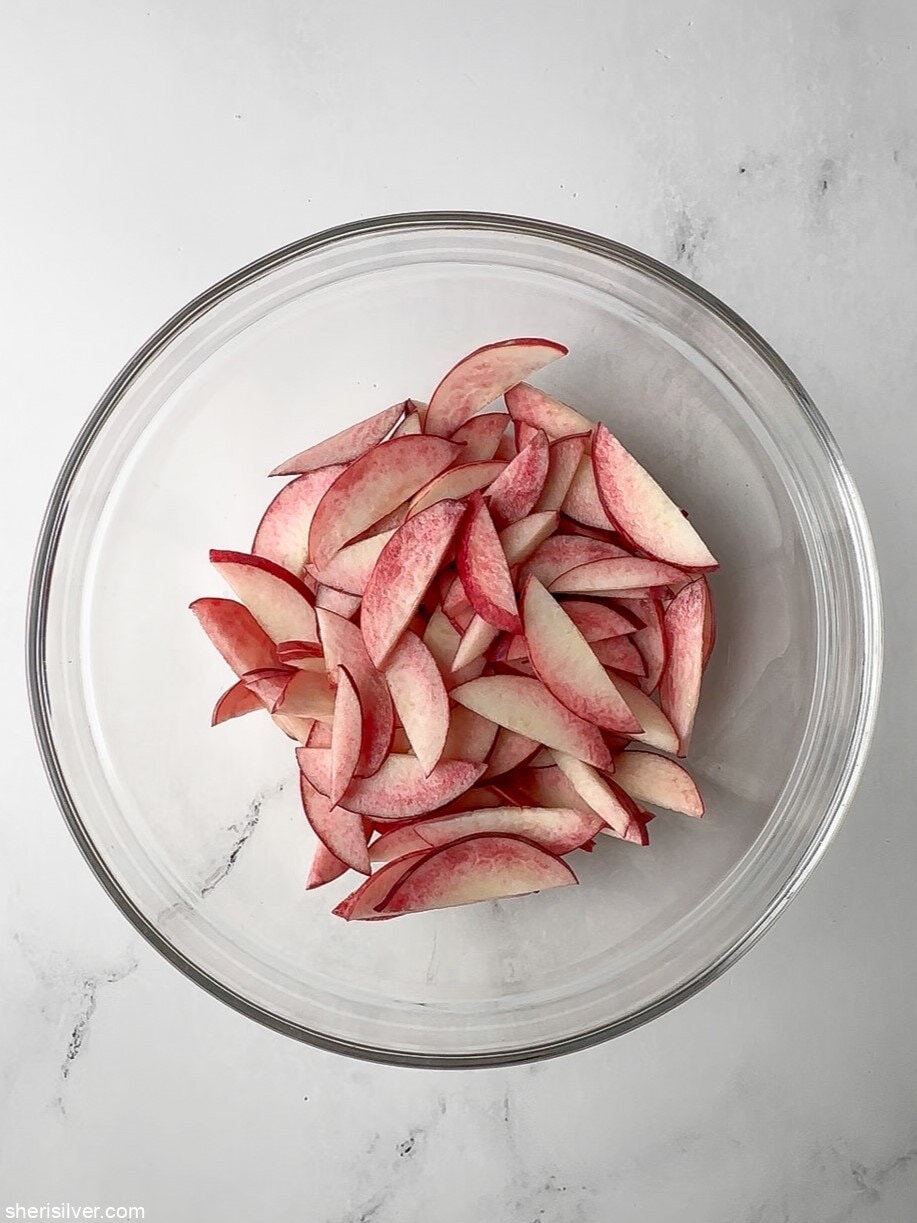 sliced peaches for easy peach galette in a glass bowl