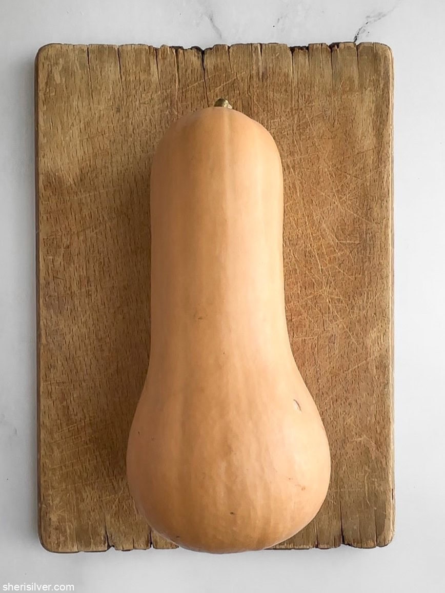 Whole butternut squash on a wooden cutting board, ready to be prepped for salad