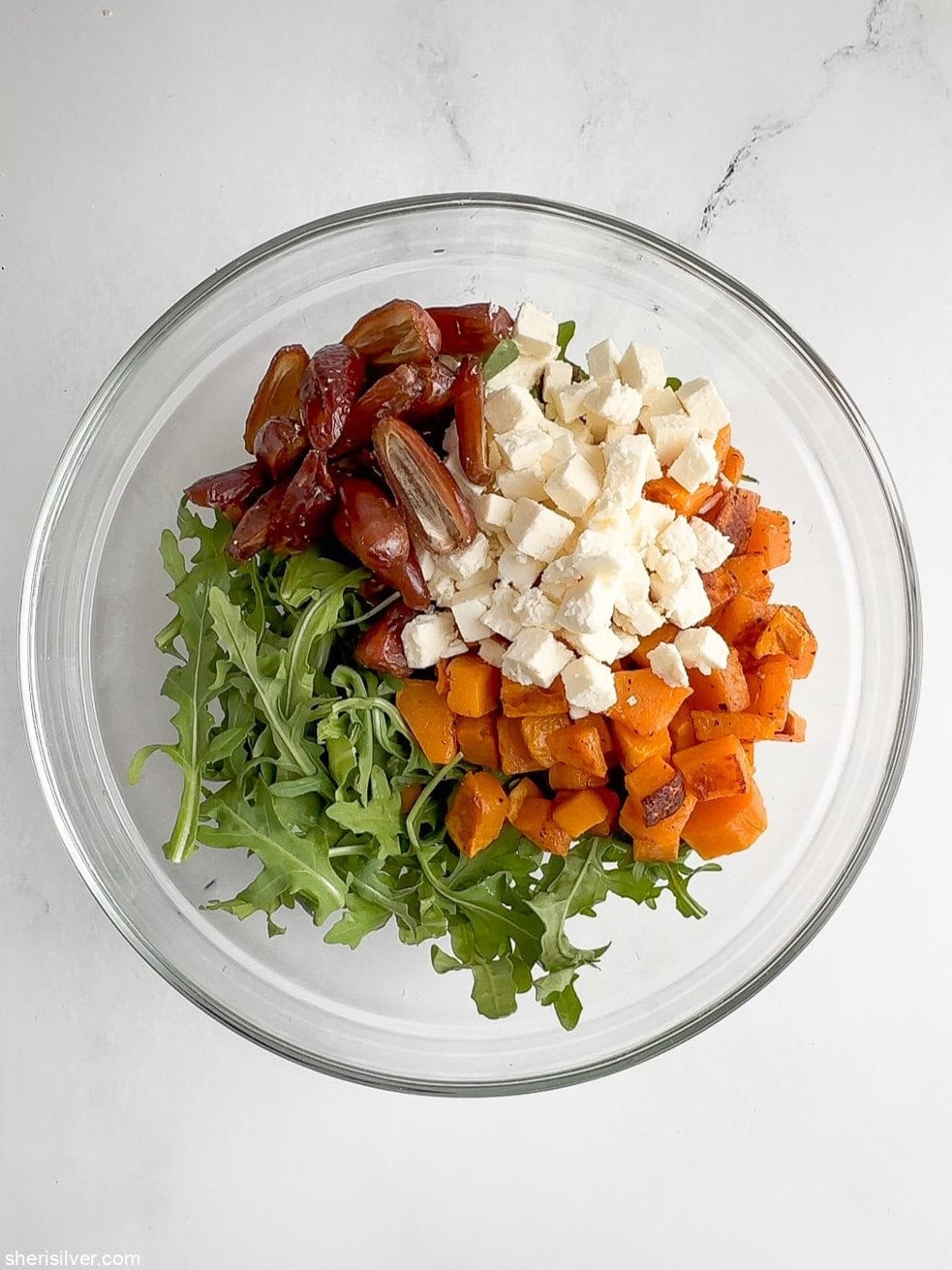 Butternut squash salad with arugula, dates, and crumbled feta in a glass bowl