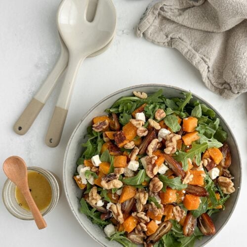 Finished butternut squash salad with dates, arugula, walnuts, and feta in a ceramic serving bowl