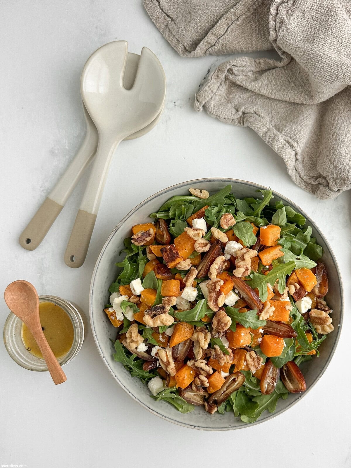 Finished butternut squash salad with dates, arugula, walnuts, and feta in a ceramic serving bowl