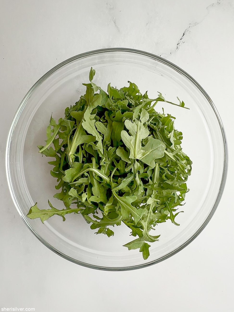 Fresh baby arugula leaves in a glass mixing bowl