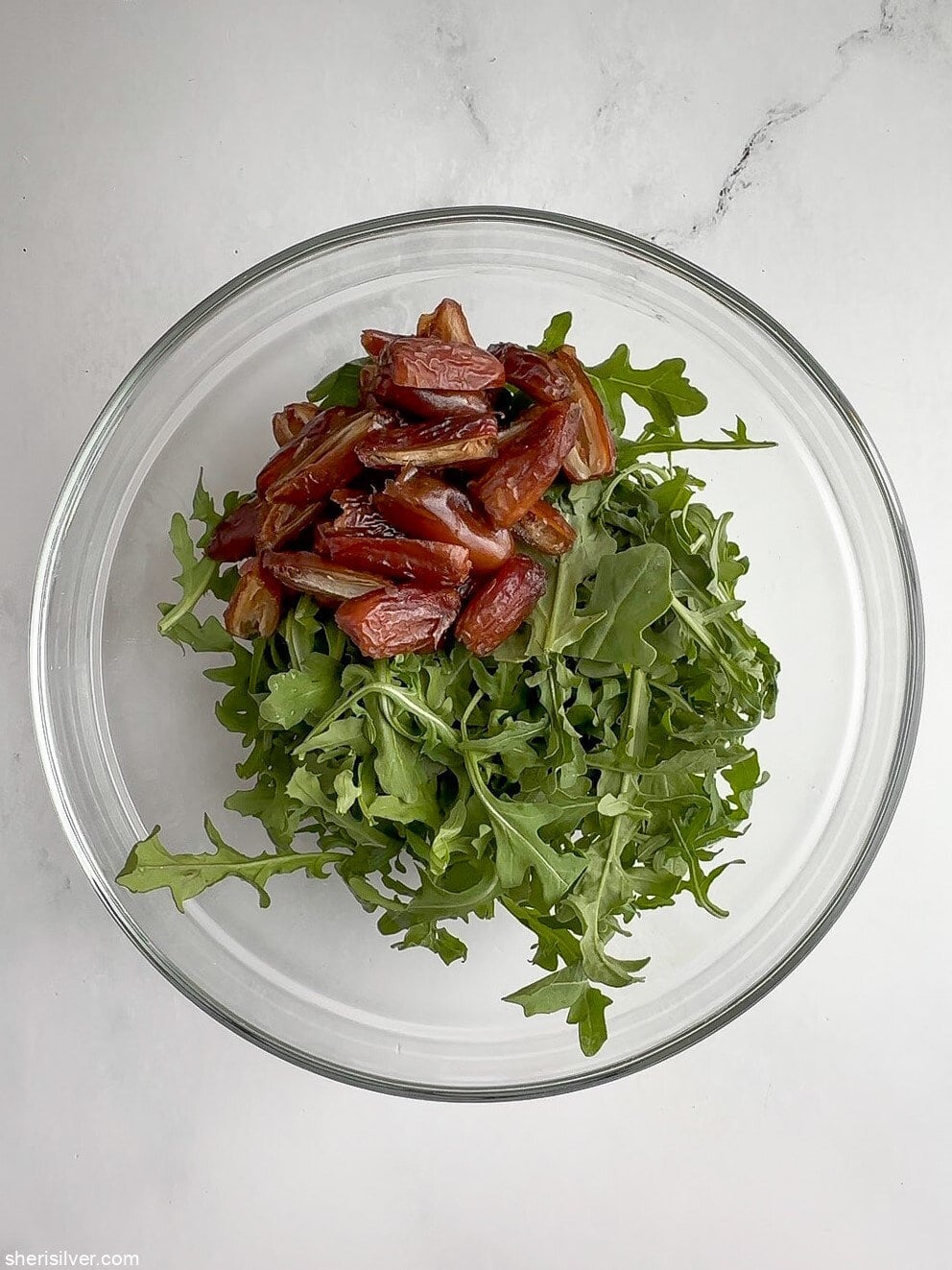 Baby arugula and halved Deglet Noor dates combined in a glass bowl