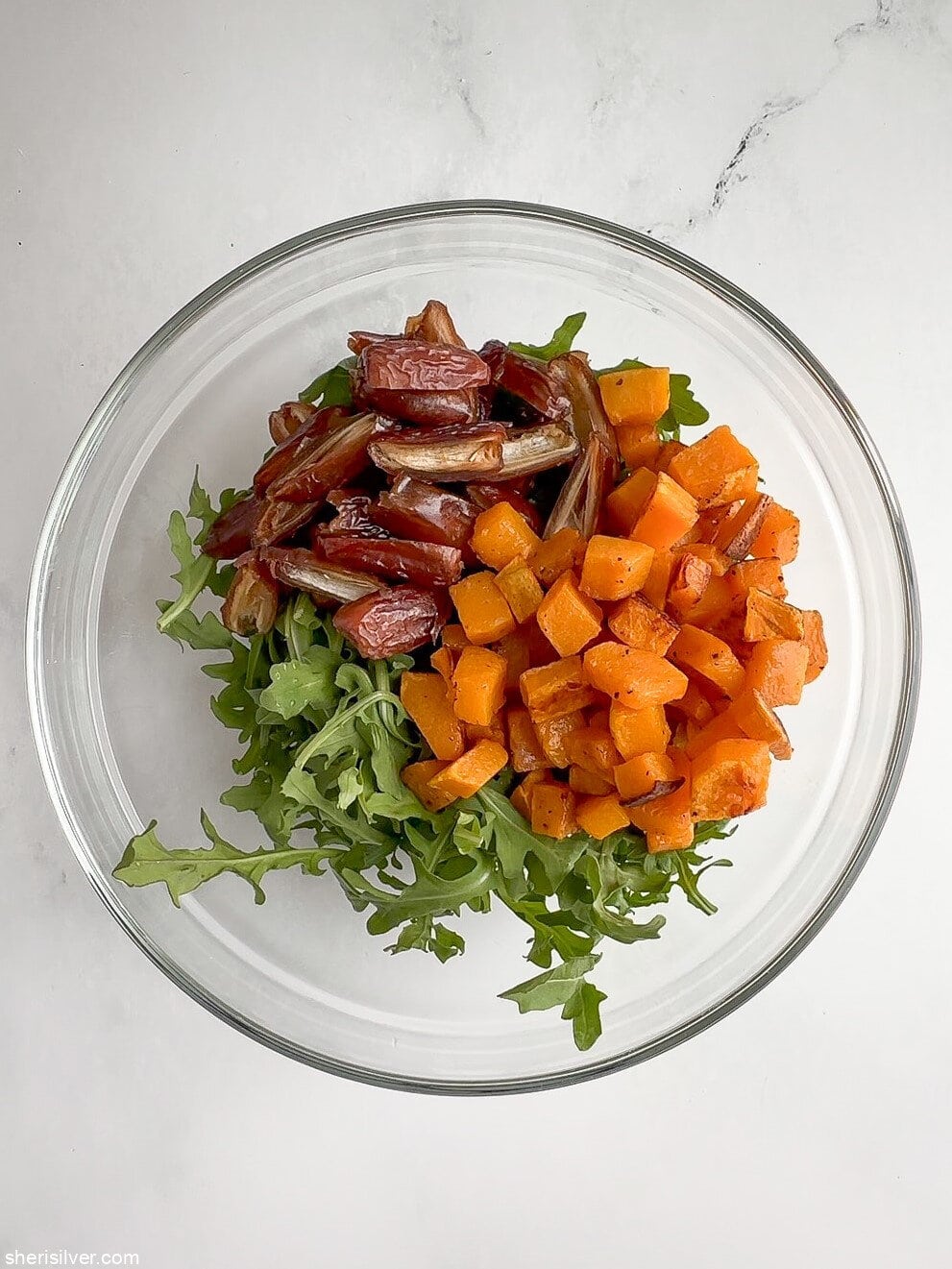 Arugula, roasted butternut squash, and dates tossed together in a salad bowl