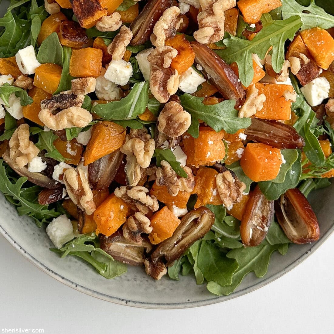Finished butternut squash salad with dates, arugula, walnuts, and feta in a ceramic serving bowl