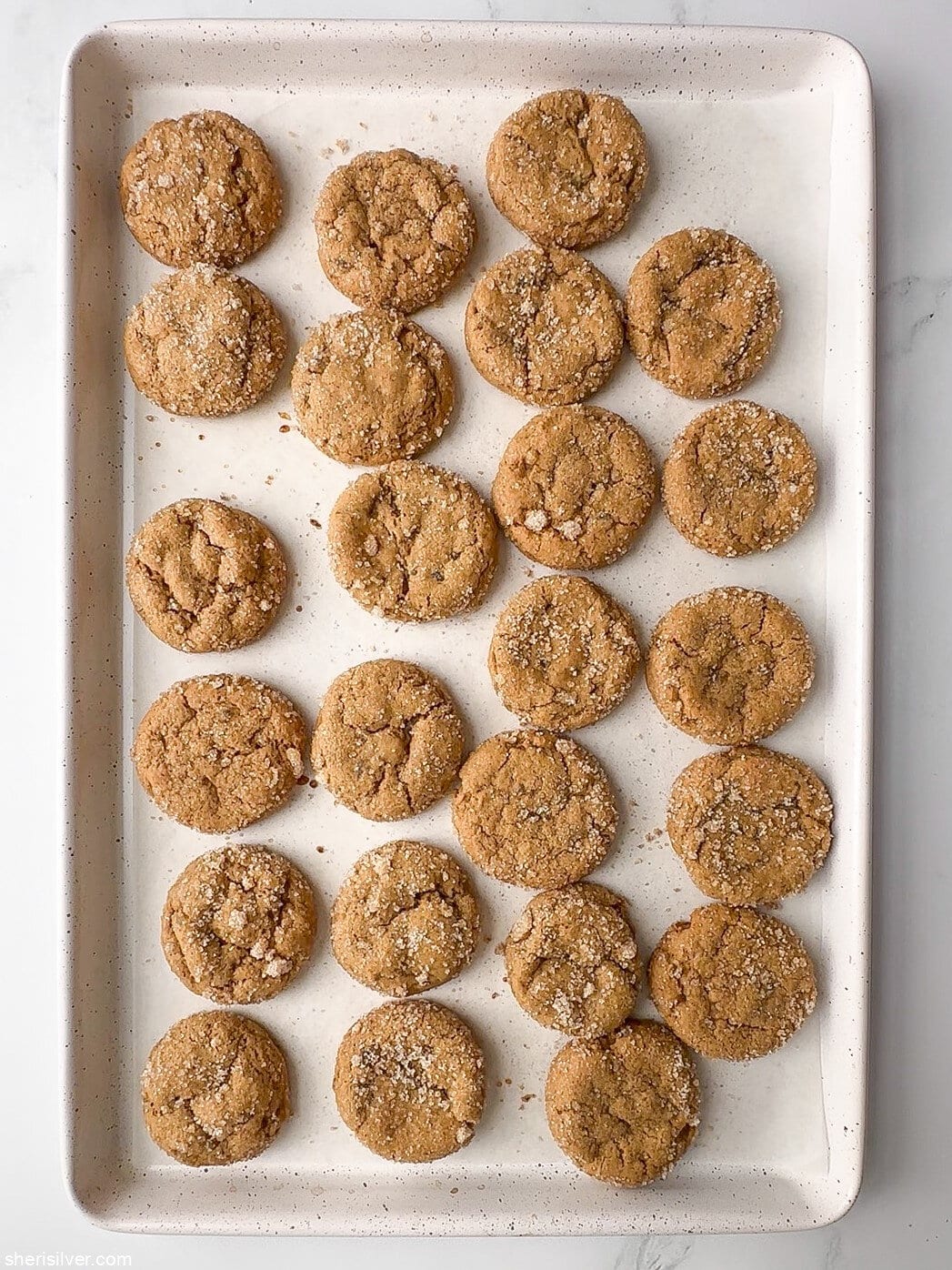Freshly baked chewy pumpkin cookies with candied ginger on a white baking sheet.