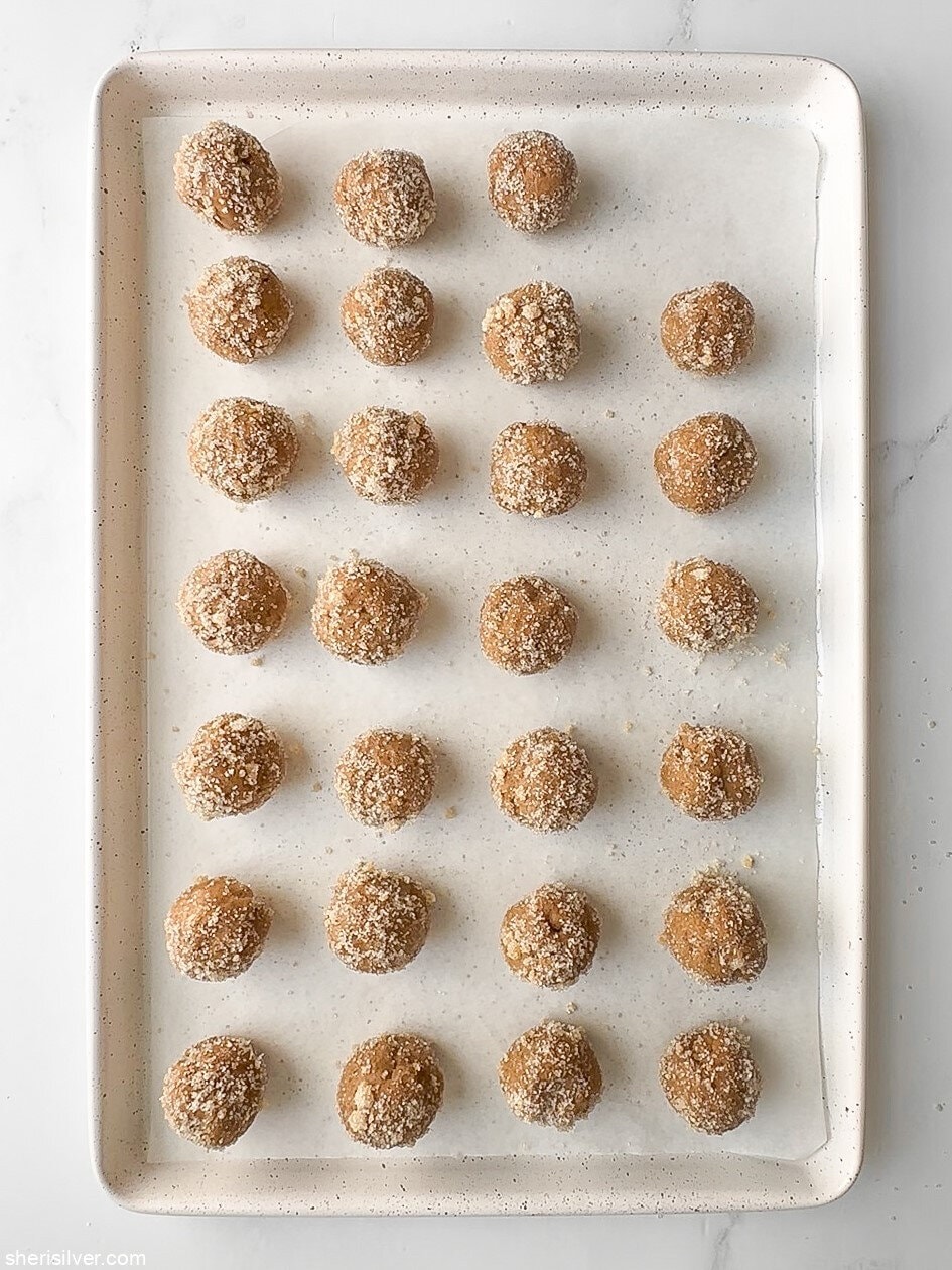 Pumpkin cookie dough balls coated in orange-ginger sugar on a parchment-lined baking sheet, ready to bake