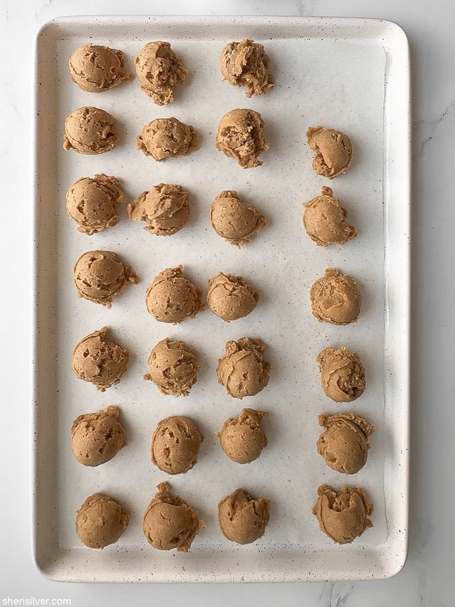 Pumpkin cookie dough scoops arranged on a parchment-lined baking sheet before rolling in sugar