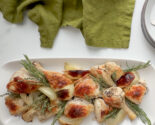 Oven roasted chicken pieces with onions, garlic, and fresh herbs on a white ceramic tray with thyme and rosemary.