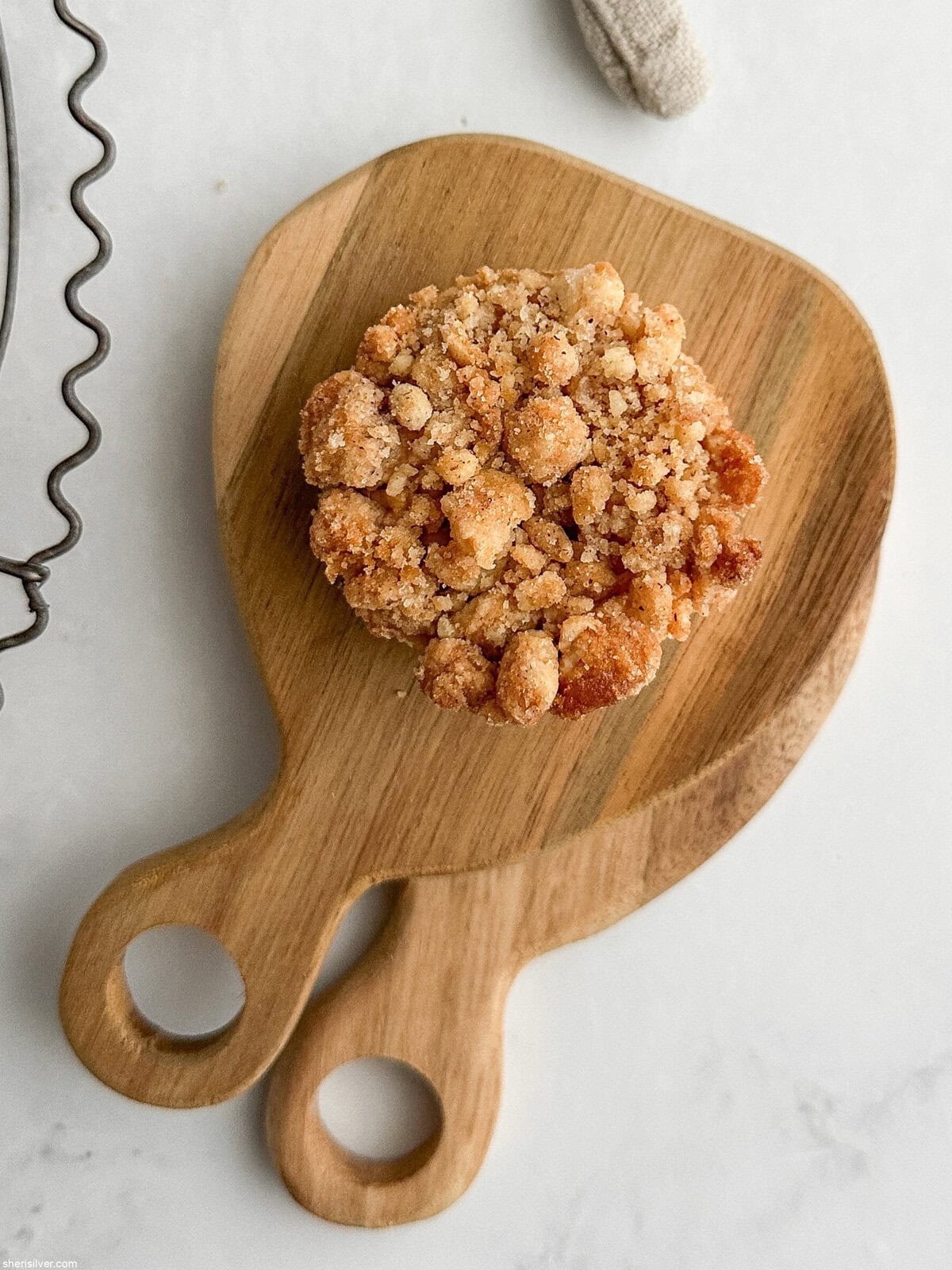 A single apple streusel pie cookie placed on stacked mini wooden boards with a soft natural linen napkin.