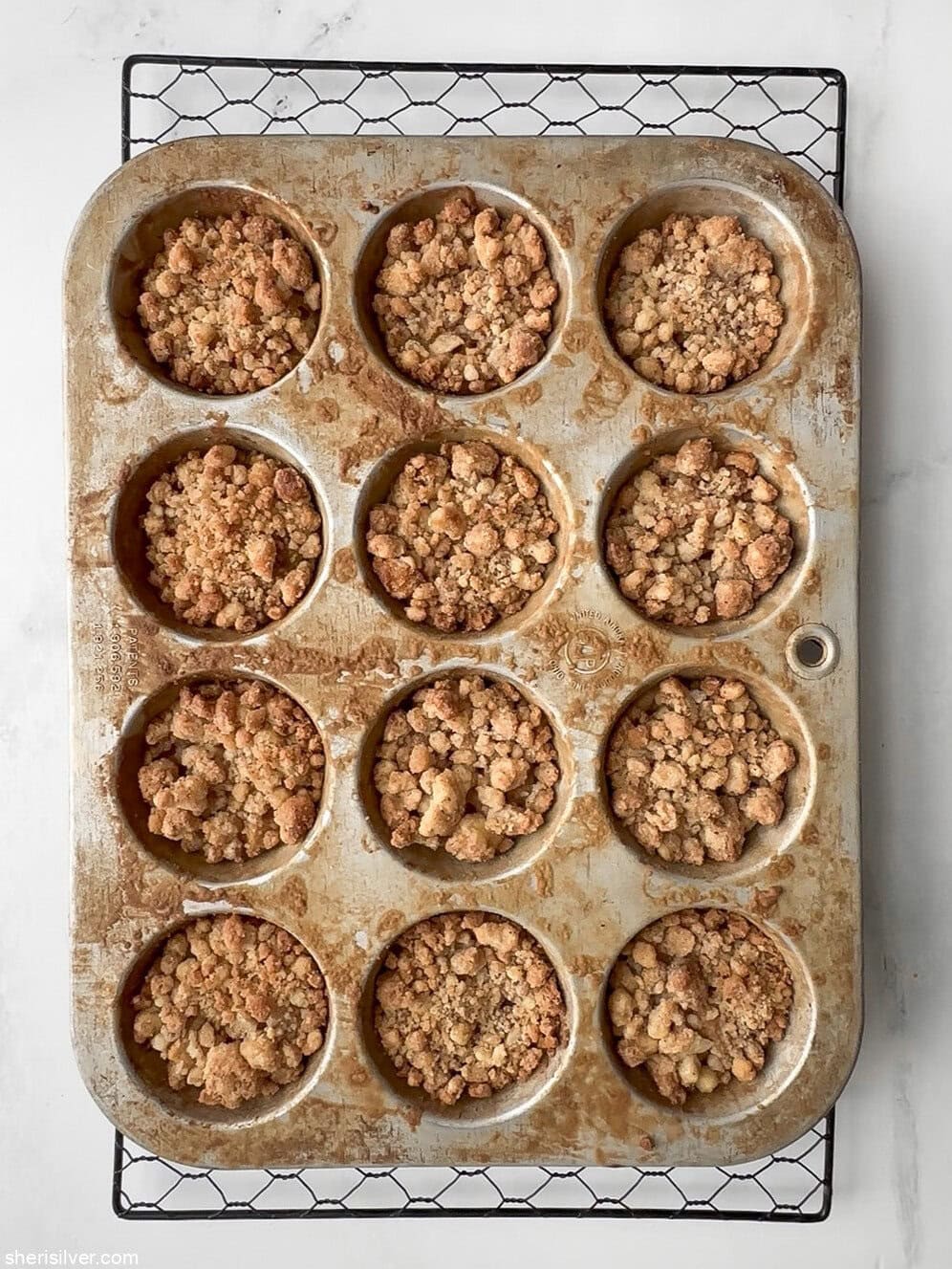 Freshly baked apple streusel pie cookies still in the muffin tin, with golden brown streusel tops.
