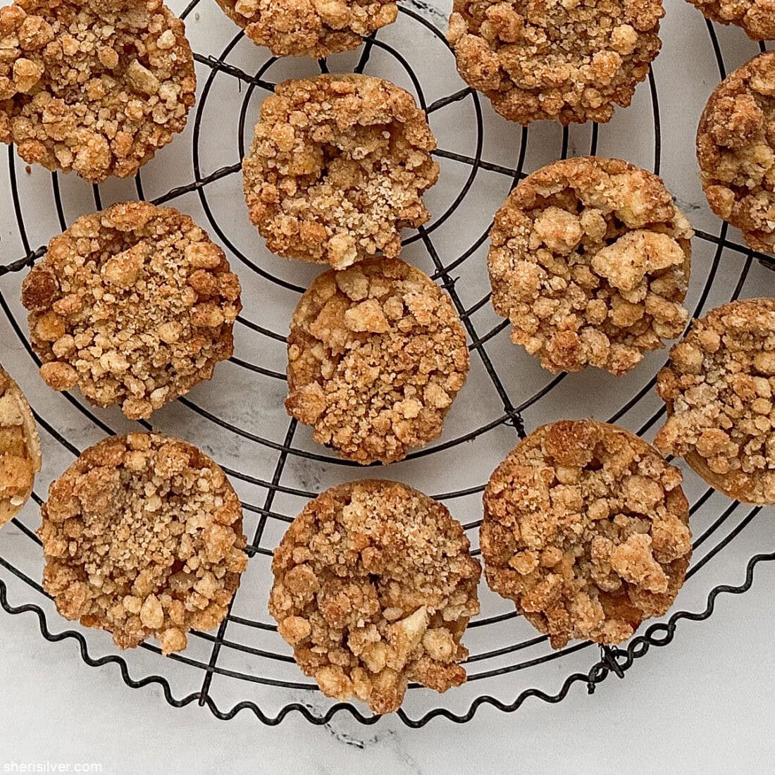 Apple streusel pie cookies arranged on a large round vintage wire cooling rack.”