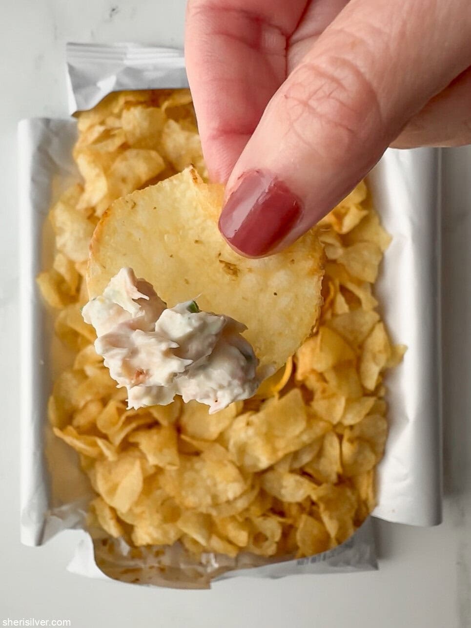 Close-up of a potato chip topped with smoked trout dip, resting over an opened bag of chips.
