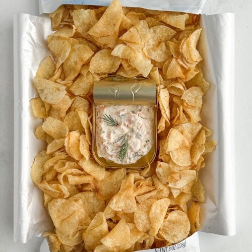 Overhead shot of a bag of potato chips laid on its back with sides opened like a tray, tin of dip nestled in the center for serving.