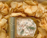 Overhead shot of a bag of potato chips laid on its back with sides opened like a tray, tin of dip nestled in the center for serving.