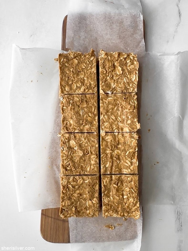 Overhead view of cut vanilla tahini protein oat bars on parchment paper on a wooden board, showing texture and thickness.