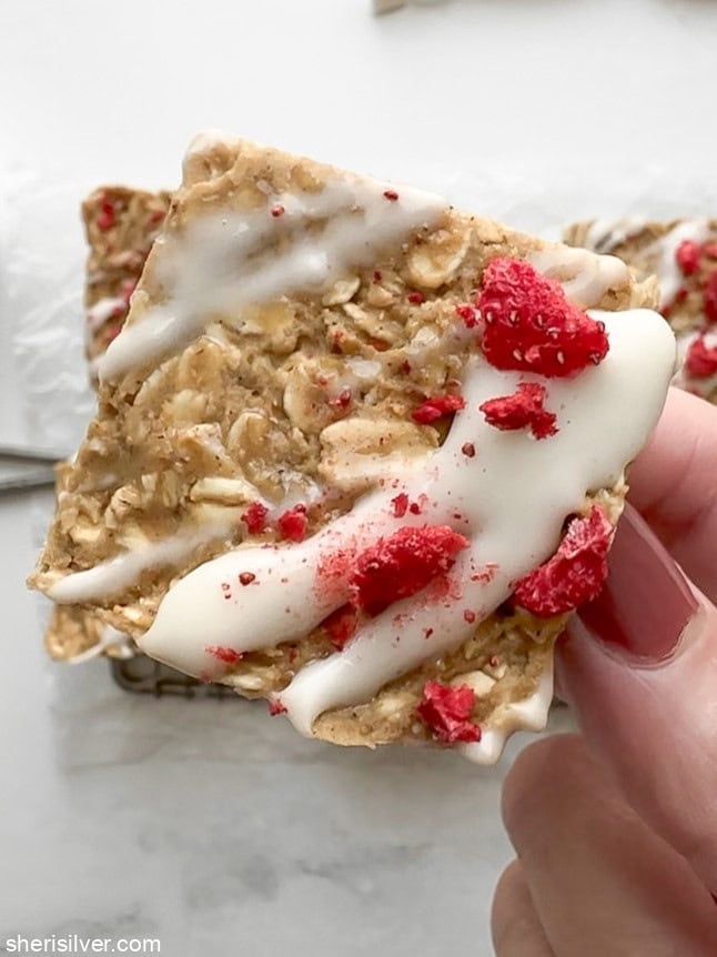 Close-up, overhead shot of a single finished vanilla tahini protein oat bar held in hand, highlighting chewy texture.