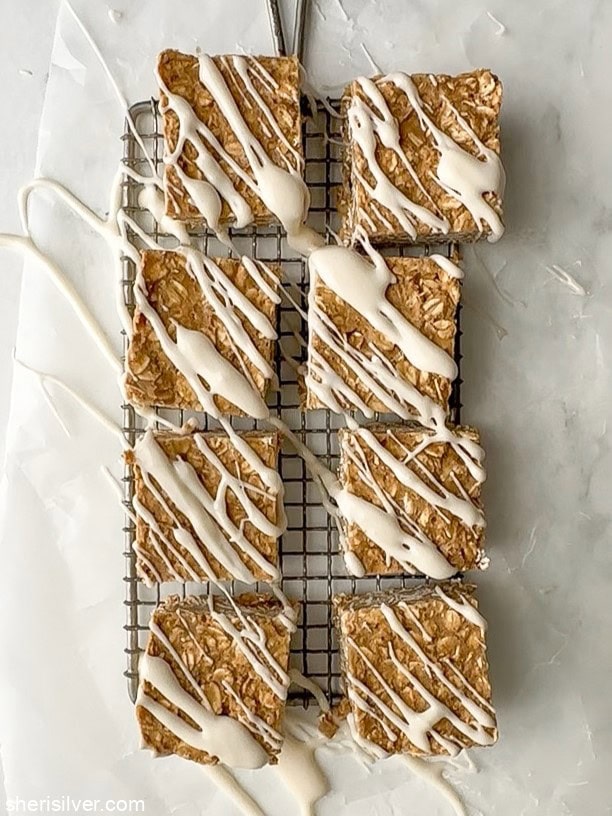 Overhead view of cut and glazed vanilla tahini protein oat bars on a small wire rack over wax paper, showing the glaze set.