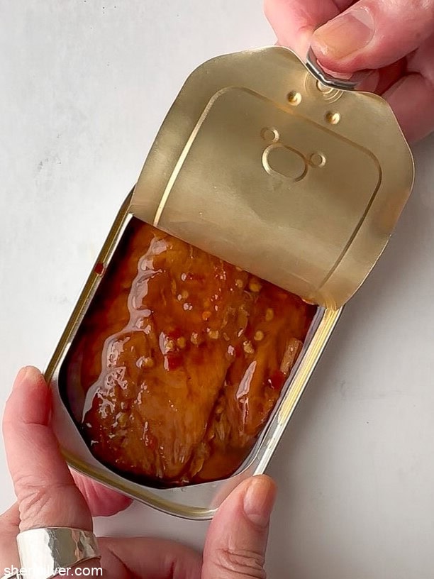 Overhead view of an opened tin of smoked mackerel with the lid partially rolled back.