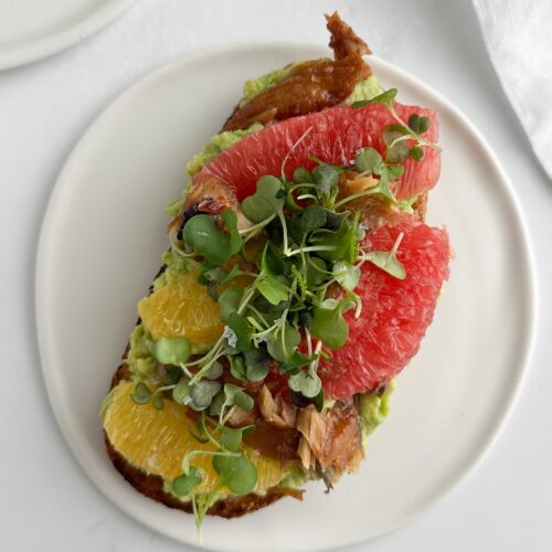 Overhead view of smoked mackerel avocado toast on a white plate.