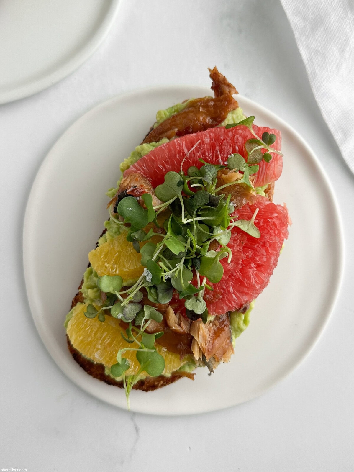 Overhead view of smoked mackerel avocado toast on a white plate.
