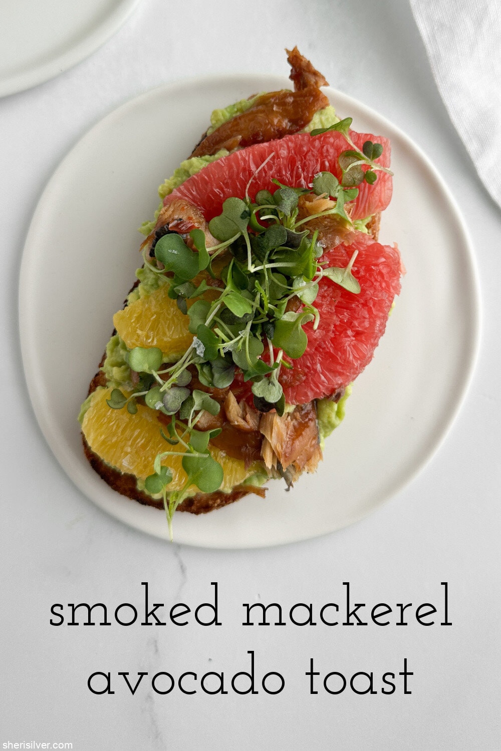 White plate topped with smoked mackerel avocado toast, shown from above with a white linen napkin.