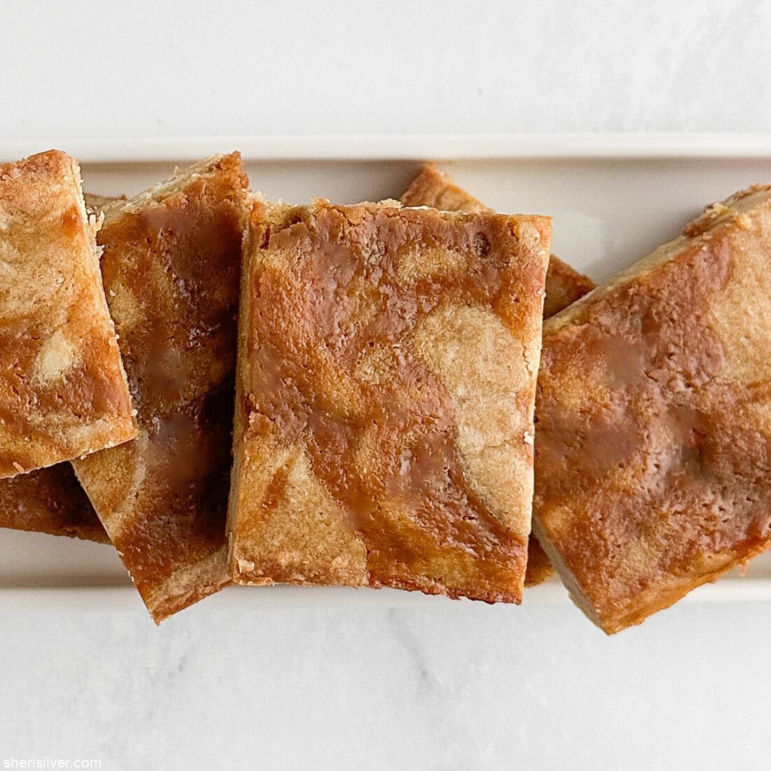 Overhead close-up of sliced blondies arranged on a white ceramic tray.