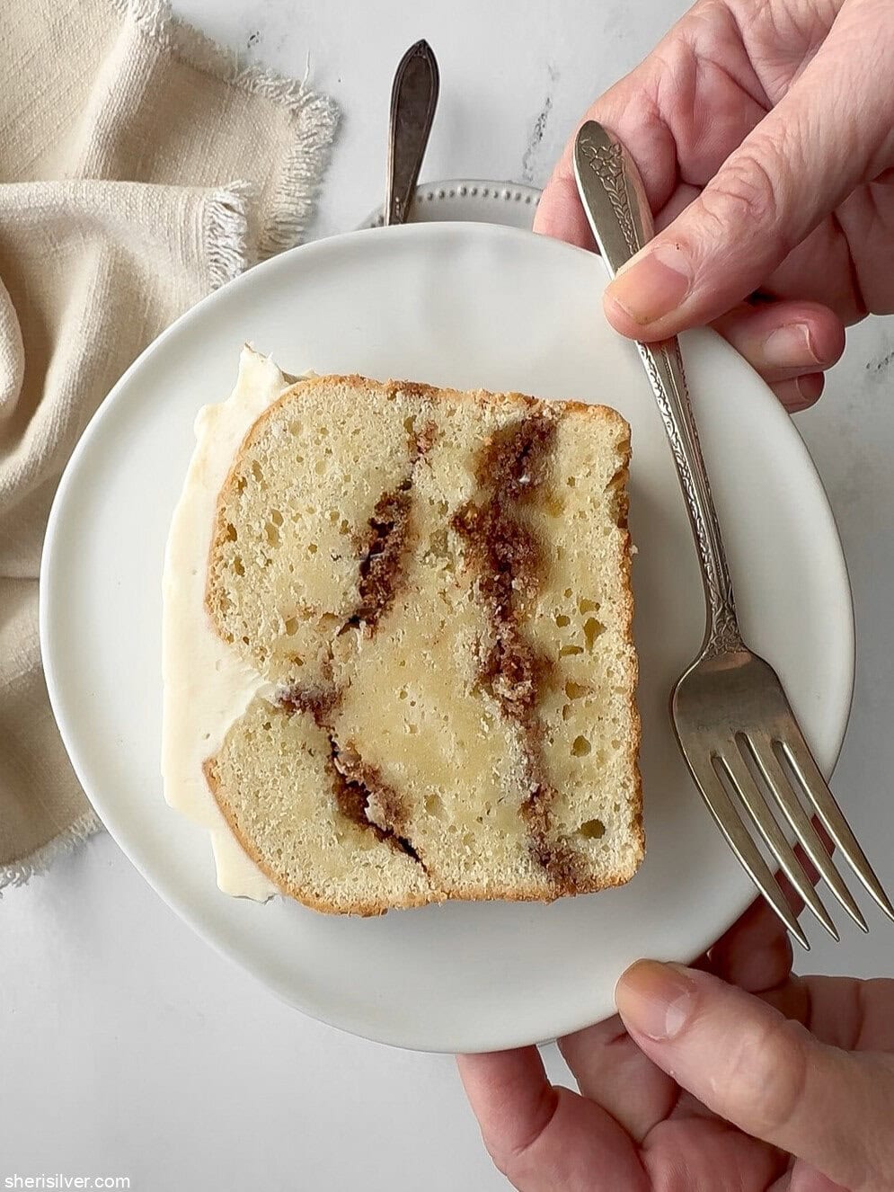 Hands holding a plate with a slice of cinnamon roll loaf cake and a vintage fork.