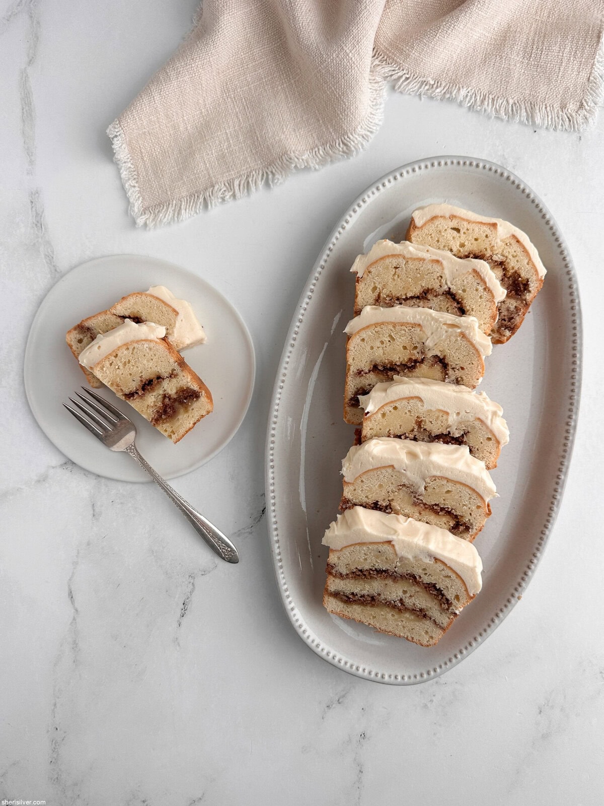 Sliced cinnamon roll loaf cake on a platter with an extra slice on a plate beside a linen napkin.