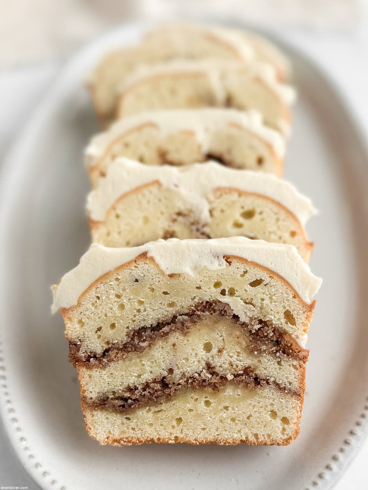 Angled view of sliced cinnamon roll loaf cake on a platter with visible cinnamon swirl layers.