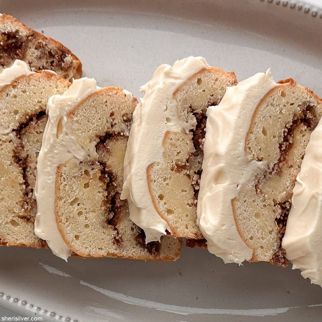 Overhead close-up of sliced cinnamon roll loaf cake on a white platter.