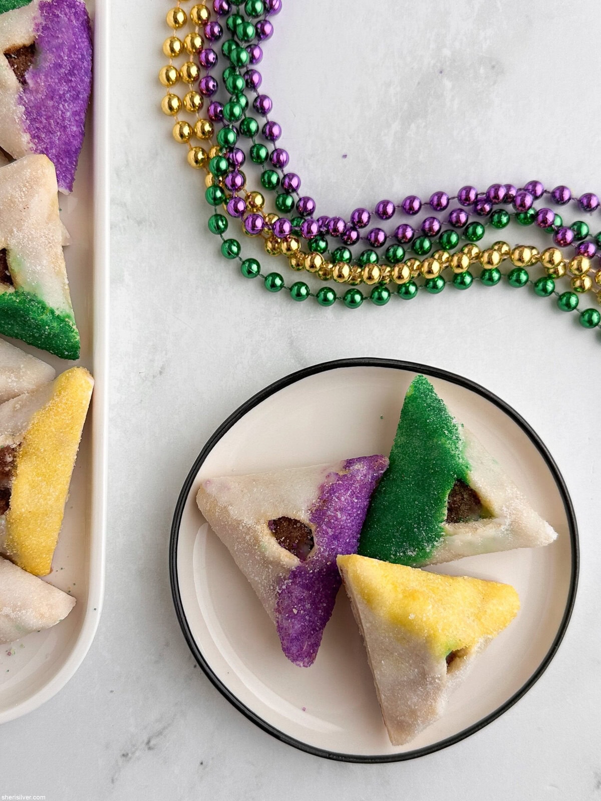 Close-up of three King Cake hamantaschen in purple, green and gold sanding sugar