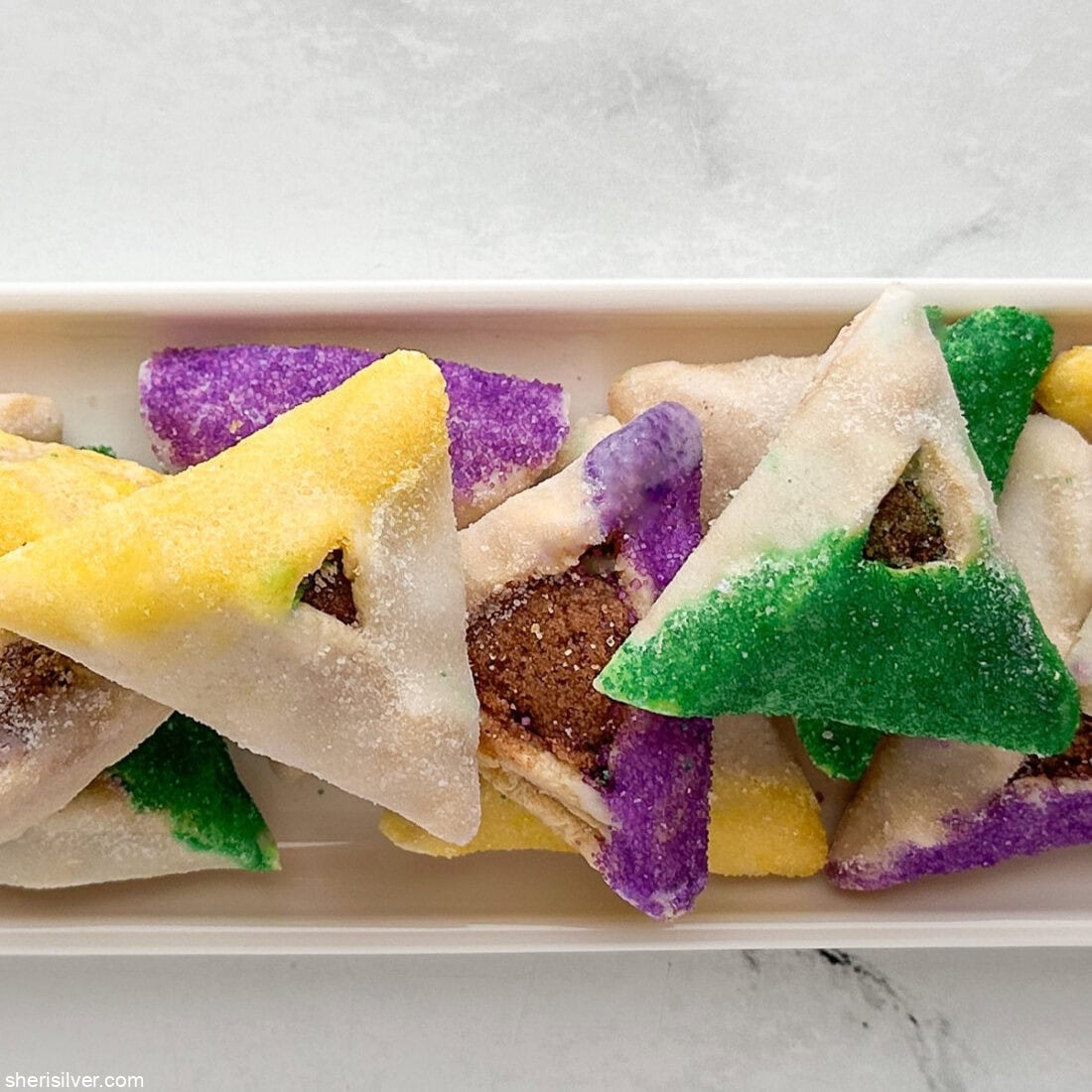 King Cake hamantaschen on a white tray with text overlay showing the recipe title