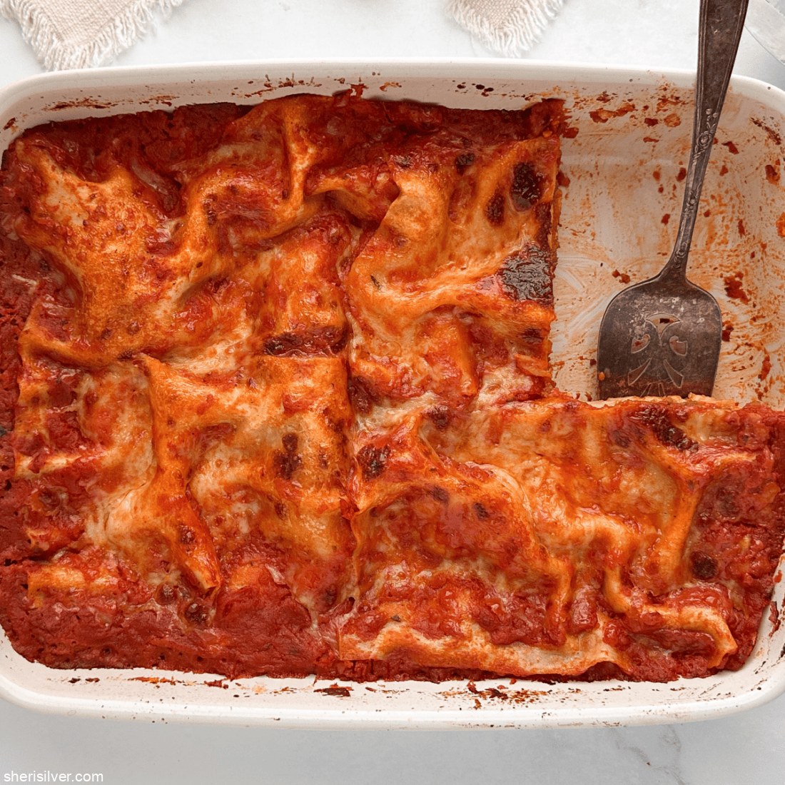 Baked lasagna in a white baking dish with one slice removed.