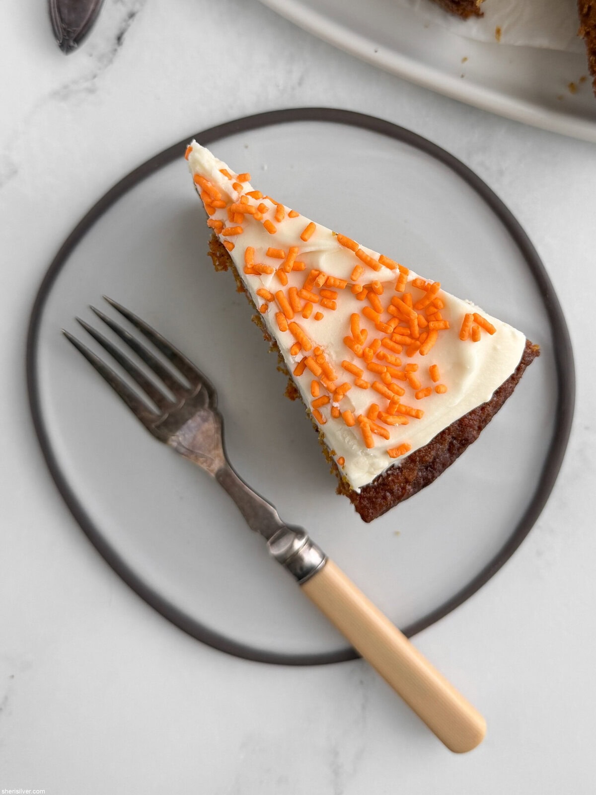 Close-up of a slice of carrot snacking cake on a white plate, showing moist crumb and frosting layer