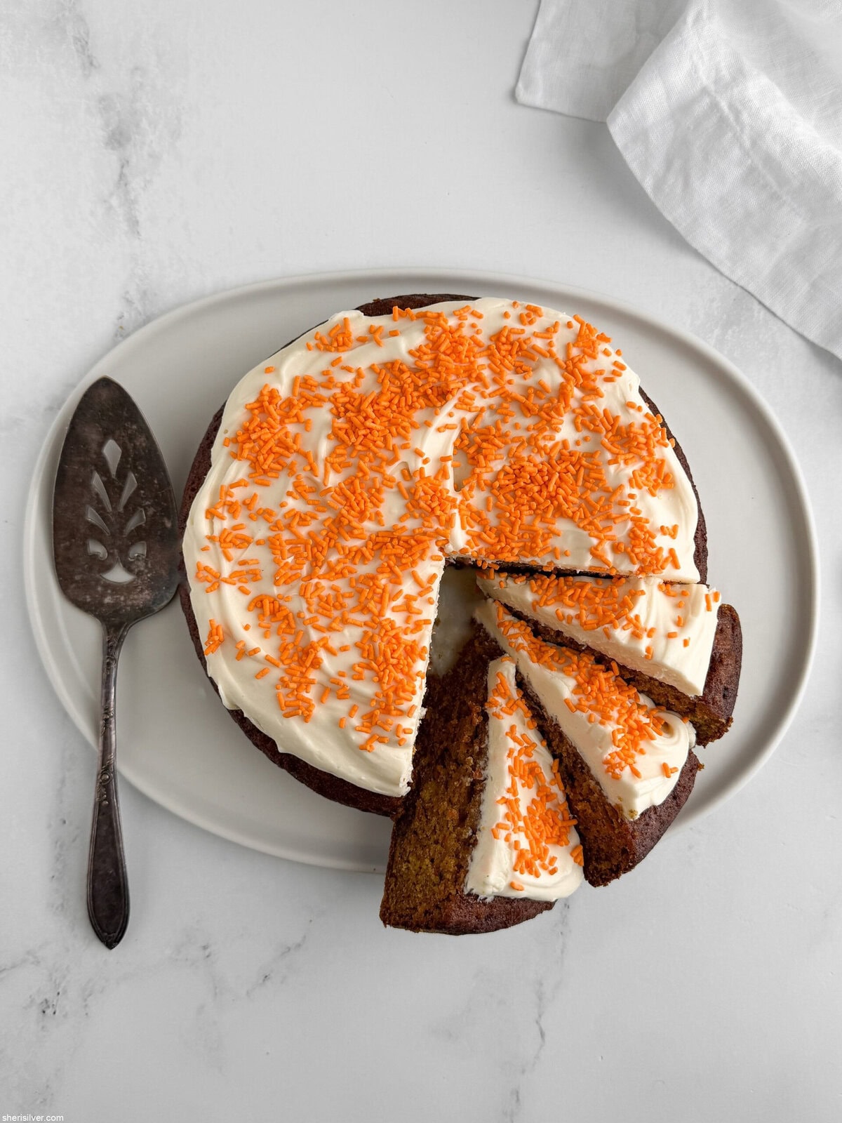 Partly sliced frosted carrot snacking cake on a white platter, highlighting texture and portioned slices
