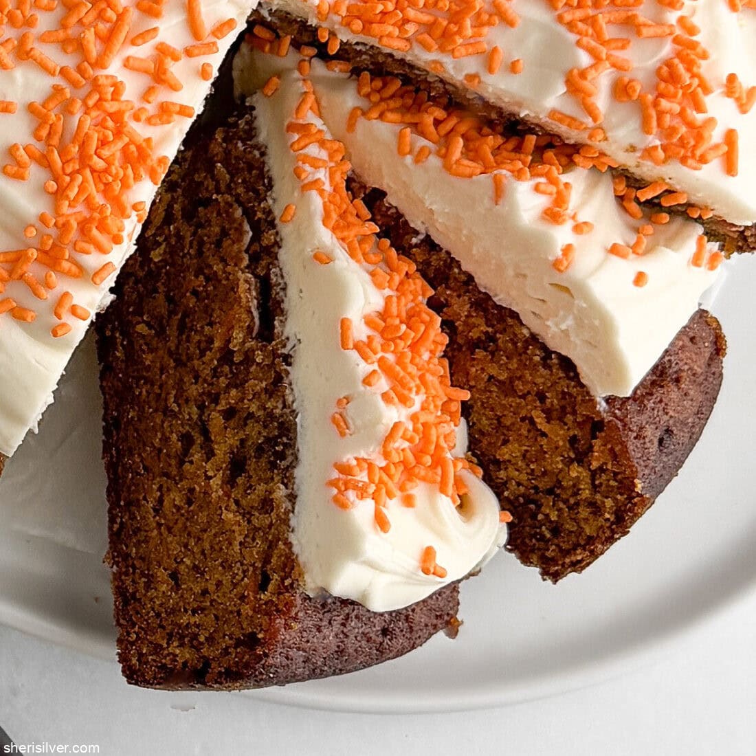 Close-up of multiple slices of frosted carrot snacking cake on a platter, showing crumb and frosting details