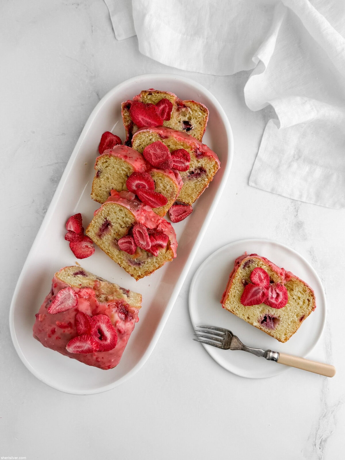 Sliced strawberry lemon loaf cake on a white platter with one slice on a side plate and a vintage fork